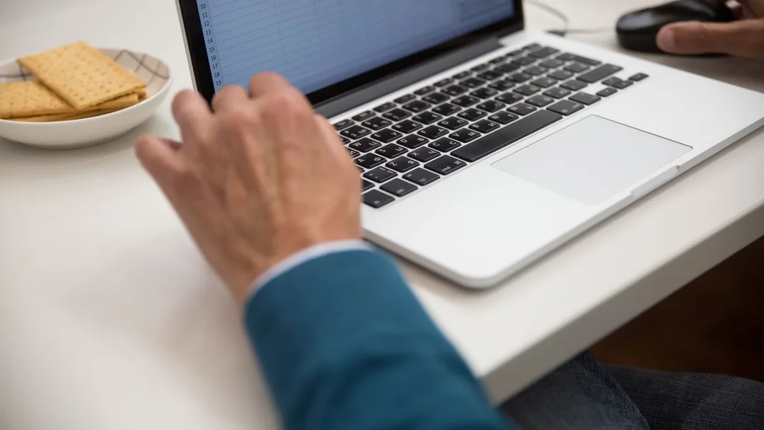 Mãos trabalhando em planilha no laptop sobre a mesa